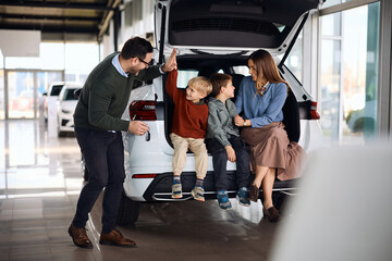 Obraz premium Happy family having fun while choosing new car in auto salon.