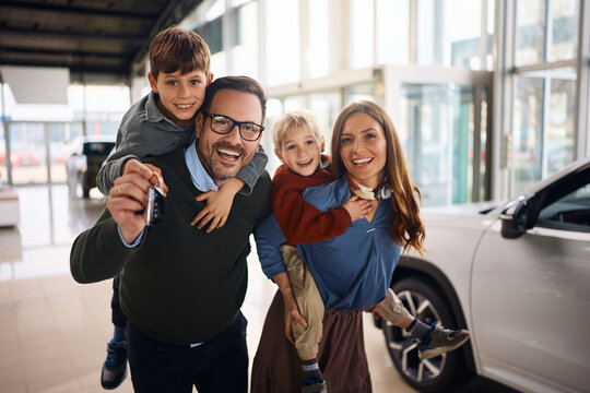 Cheerful family having fun while buying new car in auto salon and looking at camera.