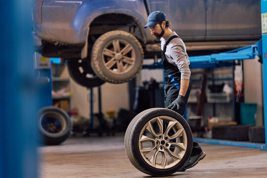 Car repairman rolling tire through garage.