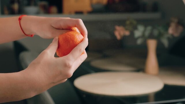 Woman peeling fresh ripe tangerine in slow motion with zest spraying, creating citrus mist. Close-up of female hands hold juicy organic fruit for healthy snack.Concept freshness, texture