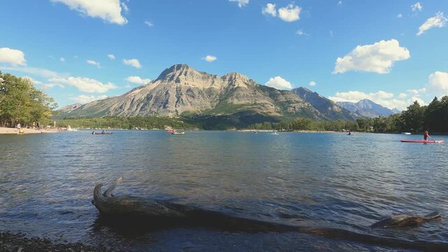 Stunning front view of a calm lake with majestic mountains rising in the background under a clear blue sky. The still water reflects the mountain peaks like a mirror, creating a peaceful and breathtak