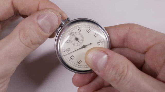 Male hands hold a silver vintage stopwatch and press the button to start the ticking hand. Concept of deadline pressure, time management, and measuring speed or efficiency.