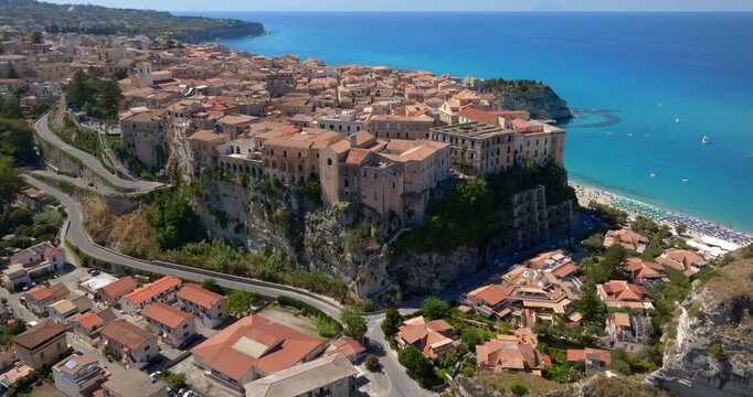 Aerial panorama of the town of Tropea, Calabria, Italy. The houses and buildings of the historic center are perched on the edge of high sandstone cliffs, overlooking the turquoise Mediterranean sea.