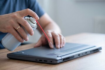 Fototapeta premium A person uses a can of compressed air to clean dust from the ventilation grills of a laptop computer.