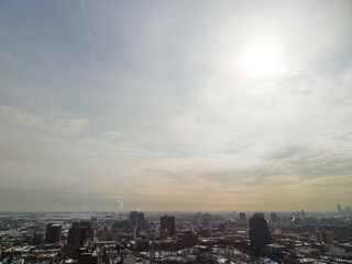 Fototapeta premium New york city skyline extending across the horizon, showcasing dense urban development with buildings and light snow cover under a bright, cloudy winter sky