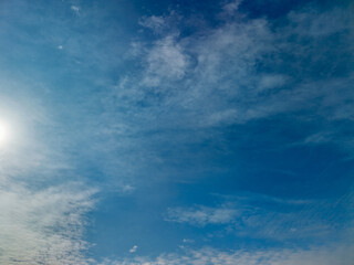 Fototapeta premium Expansive blue sky featuring soft, white wispy clouds, a bright sunburst in the upper left corner, and a clear atmospheric background representing concepts of freedom, nature, and weather