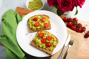 Plant-based avocado toast topped with cherry tomatoes and diced onion, photographed from above in a modern kitchen setting. The vibrant colors and minimal styling highlight fresh ingredients and conte