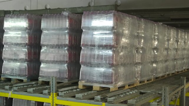 Rows of pallets with bottled beverages wrapped in shrink film in a warehouse