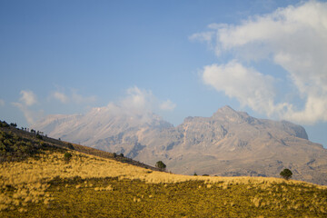 Fototapeta premium Natural highland landscape with dry meadow and mountain range under blue sky, suitable for backgrounds and environmental concepts.