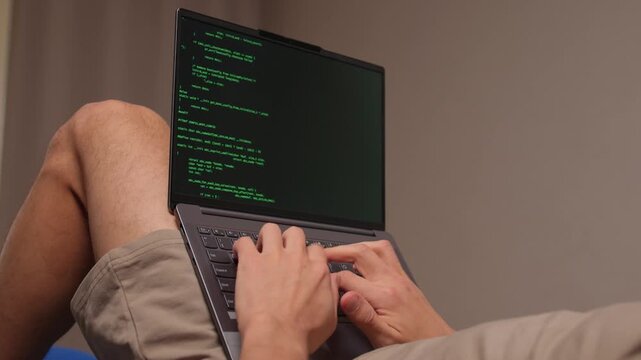 Person programming on laptop with relaxed posture and soft lighting. Individuals engaged in debugging workflow while sitting on couch in cozy environment during nighttime