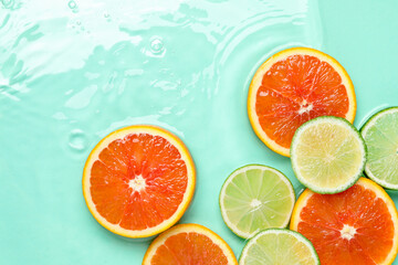 Obraz premium Slices of citrus fruits in water on turquoise background, flat lay. Space for text