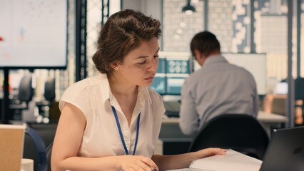 Fototapeta premium Female worker documenting essential ideas and writing on notebook, scheduling tasks and doing research for KPI. Drafting handwritten notes for business intel that reflects objectives.