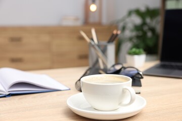 Fototapeta premium Cup of coffee, stationery, laptop, glasses and floral decor on wooden table in office, closeup