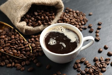 Fototapeta premium Aromatic coffee in cup and beans on black table, closeup