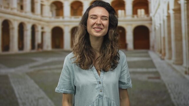 Woman showing middle finger in a sunlit building courtyard with arched corridors and worn stone floors; defiance.