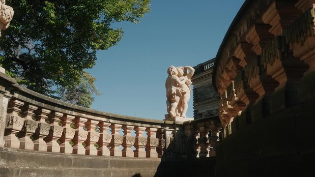 a still shoot of the statue of two putti (cherubs) located in the Zwinger Palace gardens in Dresden, Germany with tree swing in the background