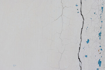 White peeling paint on the wall. Old concrete wall with cracked flaking paint. Weathered rough painted surface with patterns of cracks and peeling. High resolution texture for background and design.