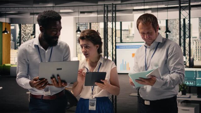 Portrait of multinational team collaborating on charts and business intelligence reports. Professionals discuss objectives, productivity and resource allocation using gadgets and office tools.