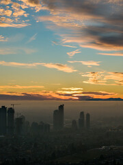 Fototapeta premium Sunset Over Burnaby Skyline With Tall Buildings and Cranes Over a Foggy City At Dusk