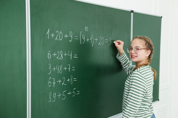 Schoolgirl doing math on chalkboard in classroom