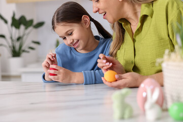 Fototapeta premium Easter celebration. Mother and her daughter painting eggs at white marble table in kitchen, closeup