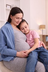 Fototapeta premium Pregnant woman and her daughter sitting on armchair at home