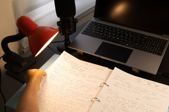 Close-up of a woman reviewing handwritten notes and studying for her final exam under a bright desk lamp at her workspace.