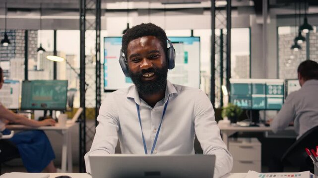 Relaxed businessman, enjoying music, short break at office, wireless headset, laptop and charts, KPI metrics and data analysis, joyful black man multitasking in a corporate environment.