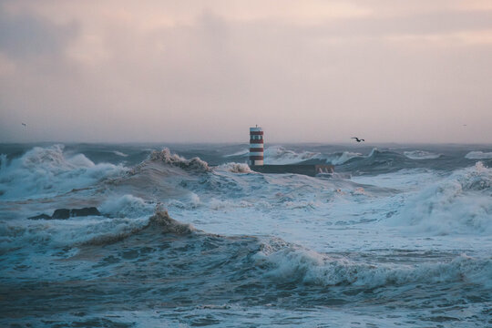 Red and white lighthouse in the middle of a stormy ocean with huge waves.