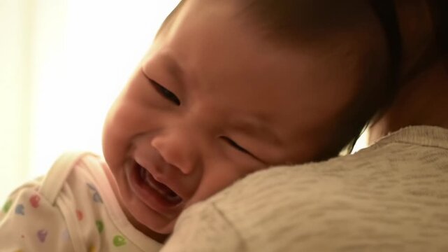 extreme close-up of a young asian baby's distressed face with tears, calming to rest on an adult's shoulder with soft light. concept of parental comfort