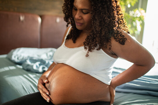 Expectant mother holding her back in sunlit bedroom