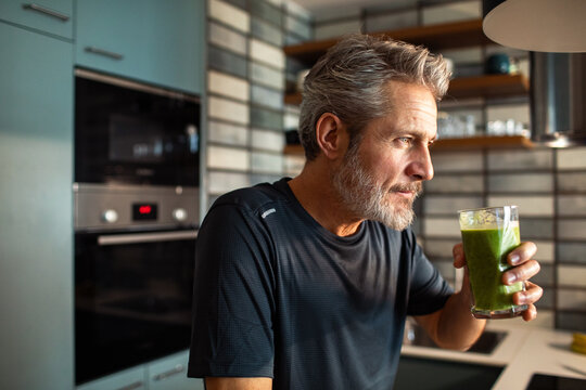 Middle aged man drinking green smoothie in modern kitchen