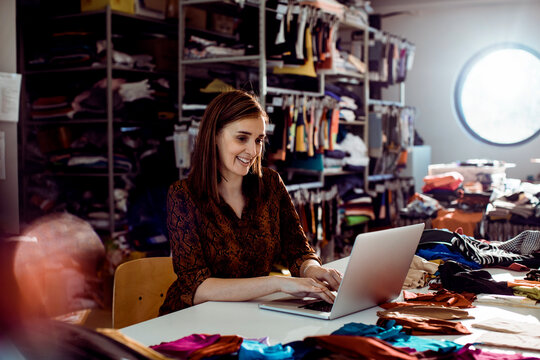 Smiling fashion designer using laptop in textile studio