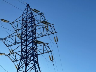 A high-voltage electricity transmission tower stands tall against a clear and bright blue sky. Concept: Concept of energy infrastructure.
