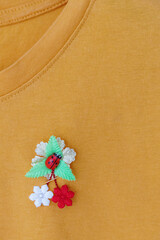 A small handmade martisor is attached to a yellow T-shirt.