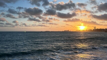 Obraz premium Golden Sunset Over Ocean Waves with Coastal City Skyline
