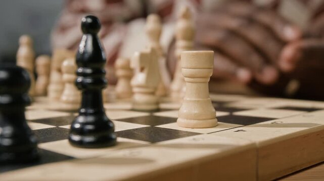 Extreme close up on hand of Black man moving rook chess piece on chessboard while playing board game indoors