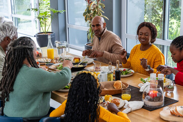 African American family sharing meal at wooden dining table, passing skillet and bread basket © wavebreak3