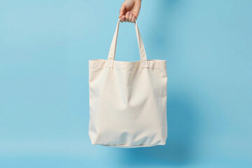 White Canvas Tote Bag Mockup Held by Hand Against Blue Background