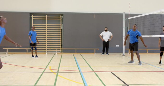 Descending volleyball leading male setter leaping under net in gym directing ball toward teammate