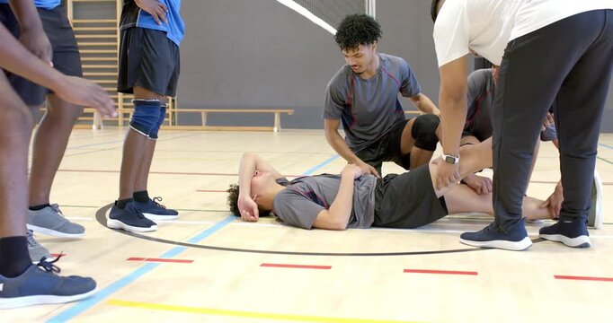 After collapse, teammates pausing on gym court rushing to Asian player testing knee helping sit up
