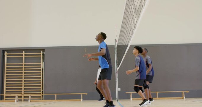Diverse volleyball team responding to toss by jumping and blocking spike and celebrating at gym net