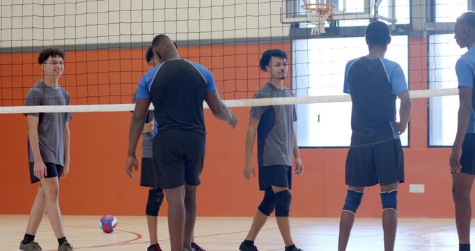 Postgame two opposing volleyball teams in jerseys gathering at gym shaking hands at volleyball net