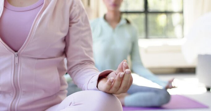 Hispanic and African American women sitting on purple mats for meditation, holding mudras by window