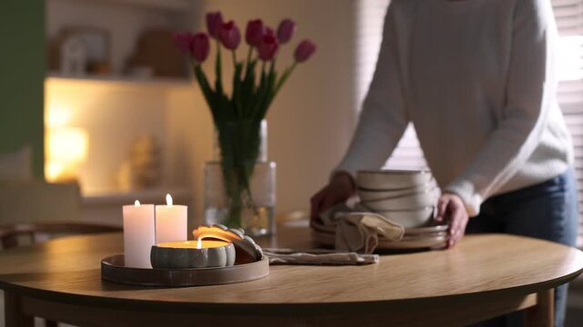Beautiful burning candles and woman putting dishes on table at home, selective focus