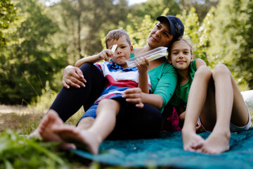 Fototapeta premium Mother with two children enjoying a summer picnic outdoors in a lush green forest clearing
