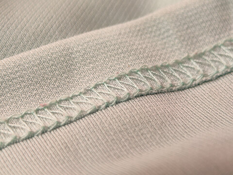 This is a close-up of a mint green shirt fabric with a teal overlock stitch seam