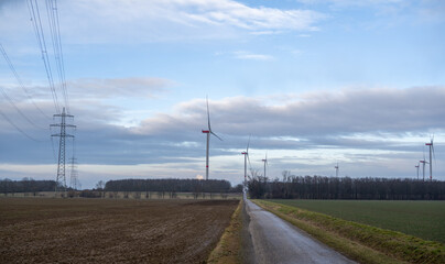 A road runs through a field with a wind farm in the background