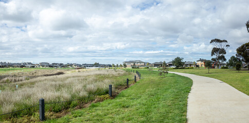 Naklejka premium A curved pedestrian path running alongside a natural wetland area in a modern suburban residential development in Australia. Urban green infrastructure, environmental planning, and outdoor parkland