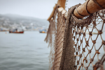 Fishing net hangs on a wooden post by the water near boats during a cloudy day in a coastal area